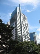 Ground-level view of a 30-storey building with protruding ledges, a spire, and a glass facade on the uppermost floors.