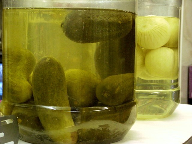 A jar of pickled cucumbers (front) and a jar of pickled onions (back)