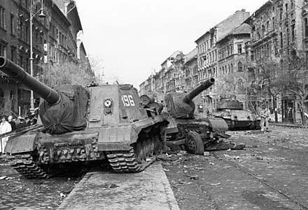 Two disabled Soviet ISU-152 assault guns in Budapest's 8th District with an abandoned T-34/85 tank in the background.