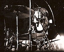 Sebuah foto hitam dan putih dari John Bonham mengenakan ikat kepala dan di belakang simbal drum kit