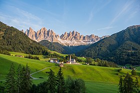 Image of a green valley with high, rocky mountains, the Dolomites, in the background