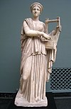 Statue von Erato, Frontalansicht; in der linken Hand hält sie eine Kithara, mit der echten greift sie herüber