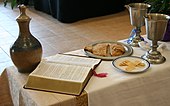 Communion setting at an ELCA service: an open Bible, both unleavened bread and gluten-free wafers, a chalice of wine, and another with grape juice EucharistELCA.JPG