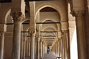 Vue intérieure du portique occidental, montrant une succession d'arcades. Celles-ci sont soutenues par des colonnes à chapiteaux de styles différents.