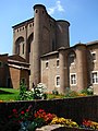 Farbfoto eines hohen quadratischen Backsteinturms, flankiert von zylindrischen Ecktürmen und halbzylindrischen Strebepfeilern.