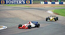 Foto de un monoplaza rojo frente a un monoplaza amarillo, en la pista