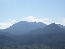 A forested landscape of low mountains, with the profile of a domed building on a distant ridgeline