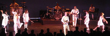 Para pemain di Byrne tur memakai semua-putih jumpsuits sambil menari, bermain alat musik, dan bernyanyi.