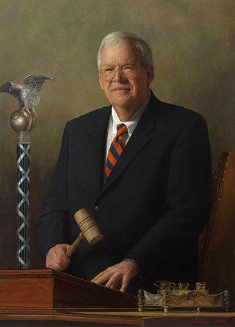 Hastert's official portrait as Speaker, painted by Laurel Stern Boeck. The mace of the United States House of Representatives is in the background, and the historic House silver inkstand in the foreground. This portrait was unveiled in 2009.[234]