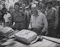 William W. Stickney cuts a Thanksgiving cake with a Japanese officer's sword at Guadalcanal, as hungry Leathernecks look on