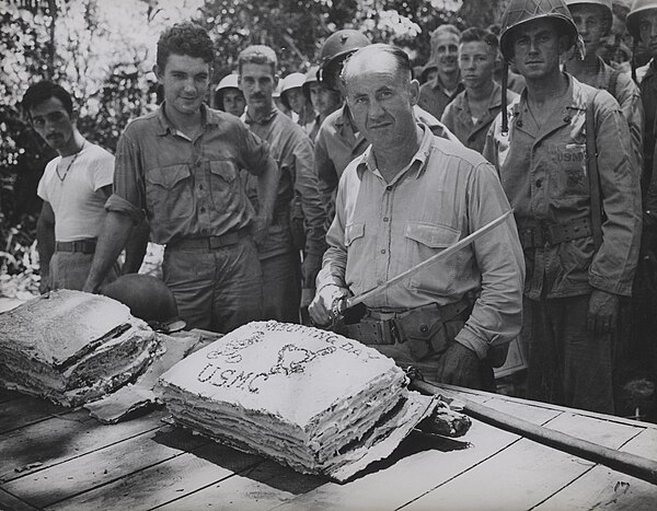 Lt. Colonel William W. Stickney cuts a Thanksgiving cake with a Japanese officer's sword at Guadalcanal, as marines of 2nd Battalion look on.