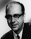 A black-and-white portrait photograph of a man wearing glasses and a suit