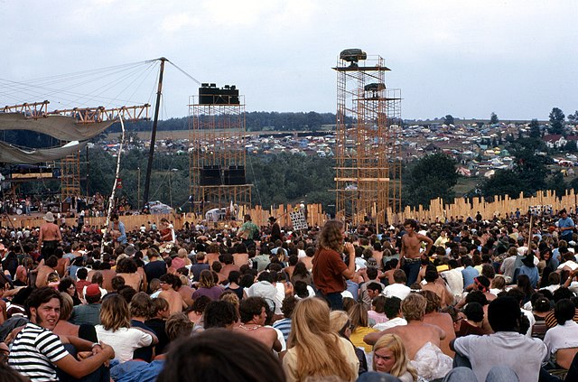 Joe Cocker performs on stage at left before crowd and huge lighting/sound towers.