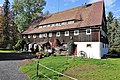 Mühlenanwesen (Ölmühle): Wohnstallhaus (Umgebinde) mit zwei Wirtschaftsgebäuden, Ölstampfe, Mühlteich und Radkastenanlage, vor dem Haus Granit-Wassertrog