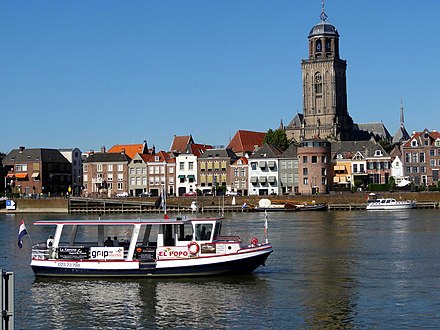 A view of Deventer's IJsselkade with the Lebuïnuskerk peering over the buildings. In the foreground the ferry linking the city centre with De Worp.