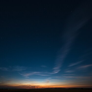 The Big Dipper emerging out of the darkness over wind turbines vanishing with the last light of the day.