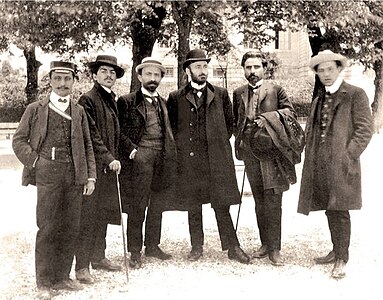 Photographie en noir et blanc de six hommes debout dans un parc.