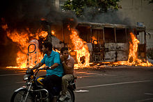 A bus burns on the streets of downtown Tehran as protesters cycle by on 13 June Burning bus, Iranian presidential election 2009.jpg