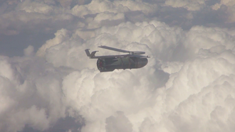 Eine Fliegerbombe, die mit einer Tragflügelbaugruppe zur Gleitbombe aufgerüstet wurde, im Flug über den Wolken