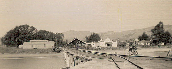 Old Hearst pier (built 1878) and the San Simeon waterfront, c. 1890s. Wooden warehouse and employee residence, next to rail line (dark wood) are at ce