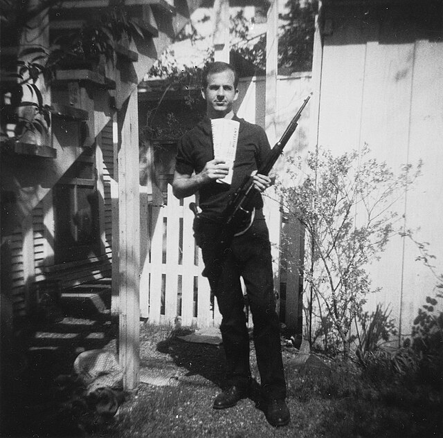 A photograph of Oswald posing with his rifle, holstered pistol, and communist literature