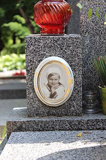 Fotografie chlapce v malém zlatavém rámečku umístěná na kamenném pomníku hrobu.