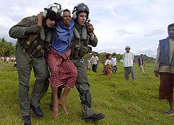 Naval Air crewmen carry a seriously injured Indonesian woman to a medical facility