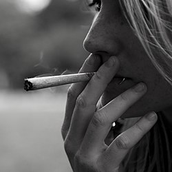En ung kvinne med lyst hår som røyker en joint (cannabissigarett).