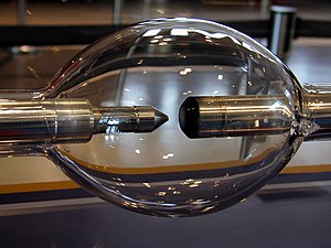 Elongated glass sphere with two metal rod electrodes inside, facing each other. One electrode is blunt and another is sharpened.