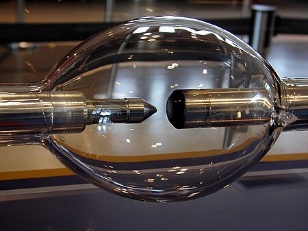 Elongated glass sphere with two metal rod electrodes inside, facing each other. One electrode is blunt and another is sharpened.