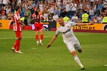 Photo de Karim Benzema courant les bras écartés sur un terrain de football vêtu du maillot du Real Madrid.