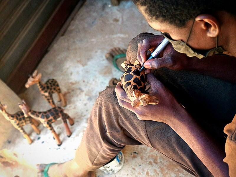 File:Boy painting a wooden giraffe statuette 02.jpg