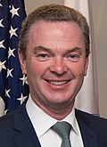 Christopher Pyne'nin Amerikan bayrağının önündeki kameraya bakan fotoğrafı