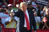 Trump señala con el dedo en un mitin de campaña, con multitudes detrás de él