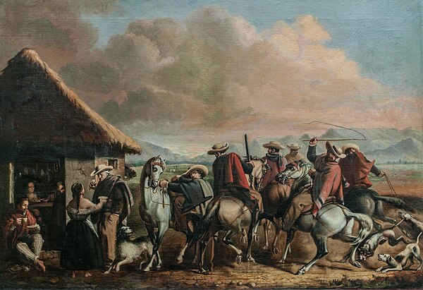 A group of Venezuelan hunters wearing the countryman cavalry attire from the region with a Bahareque house.