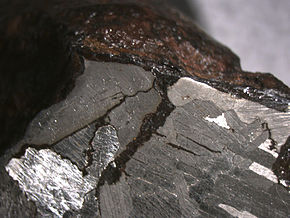 Eisenmeteorit (Mundrabilla/Australien). Er wurde geteilt, die Schnittfläche geschliffen und geätzt. Unter dem Mikroskop sind deutlich die Widmanstätten’schen Figuren (ca. 3 mm lang) und die Verwitterungsrinde zu erkennen.