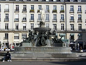 La fontaine monumentale de la place, se détachant devant une façade d'immeuble blanche
