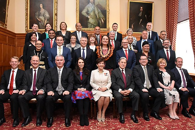 De regering van Nieuw-Zeeland na beëdiging in 2017. Generaalgouverneur Patsy Reddy zit middenvoor; ze wordt door Jacinda Ardern (links) en Winston Peters (rechts) geflankeerd.