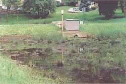 Peat-sand filter in United States. The filter treats stormwater runoff from a residential area. Stormwater from streets is first routed to a small detention basin (rear of photo, behind berm), which removes coarse sediment. After filtration an under-drain piping system discharges the filtered water to an adjacent stream. Peat sand filter.jpg