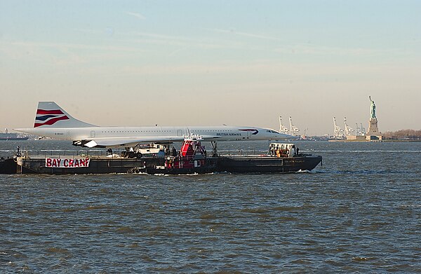 A British Airways Concorde being towed in New York City, USA. It is on a deck barge.