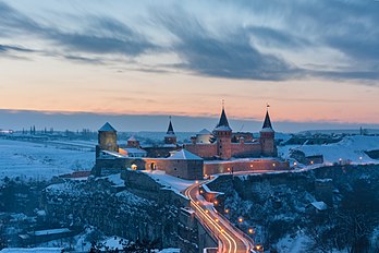 Castelo Kamianets-Podilskyi, inicialmente construído para proteger a ponte que liga a cidade ao continente, o castelo fica no topo de uma península esculpida pelo sinuoso rio Smotrych, formando um sistema de defesa natural para o histórico bairro da Cidade Velha de Kamianets-Podilskyi. A sua localização num cruzamento estratégico de transportes na Podólia fez do castelo um alvo privilegiado para os invasores estrangeiros, que o reconstruíram de acordo com as suas próprias necessidades, acrescentando à sua diversidade arquitetônica multicultural. Especificamente, o complexo consiste: da Cidade Velha fortificada pelo rei Casimiro IV, do Castelo Velho reconstruído pelos reis Sigismundo I e Estêvão Báthory, e do Castelo Novo fundado pelos reis Sigismundo III e Ladislau IV. No entanto, apesar das muitas mudanças arquitetônicas e de engenharia na estrutura original, o castelo ainda forma um projeto arquitetônico coerente, sendo um das poucas construções medievais na Ucrânia moderna que está relativamente bem preservada. Junto com o bairro da Cidade Velha, o castelo está listado como parte do Santuário Histórico-Arquitetônico Nacional "Kam'ianets" e do Parque Natural Nacional Podilski Tovtry. O complexo é uma das Sete Maravilhas da Ucrânia. Hoje, o Castelo é o marco mais reconhecido da cidade, servindo como uma importante atração turística regional e nacional. (definição 3 755 × 2 500)