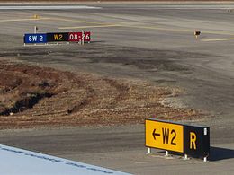 The yellow "W2" direction sign in the foreground leading to the black "W2" location sign in the background. The blue "SW 2" sign is non-standard. Ben Gurion International Airport 4 taxiway signs.JPG