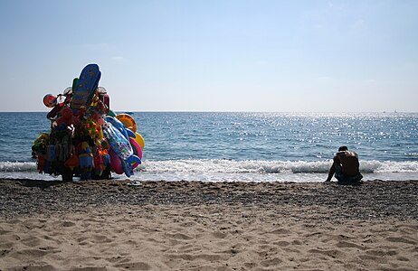 English: Beyond the sea is my home. Picture of a tired man, an immigrant, who is resting on the beach where he works (hard) with his wares. Italiano: Foto di un immigrato che si riposa durante una dura giornata di lavoro sulla spiaggia sotto il sole cocente.