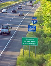 Drei Schilder entlang einer stark befahrenen Autobahn.  Der untere sagt "Entering Greenwich Connecticut".  Auf dem darüber steht "Litter Removal".  Der letzte oben ist unregelmäßig geformt mit der Nummer 684