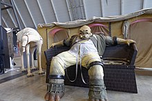Statue d'un individu allongé dans un canapé.