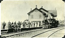 Een station met passagiers op het perron en een stoomlocomotief.