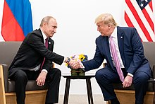 Трамп и Путин сидят, наклоняются и обмениваются рукопожатием.