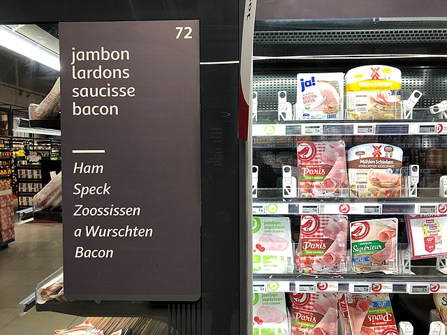 Sign in French and Luxembourgish (in italic) in a supermarket. Items labeled in Standard German and French are displayed.