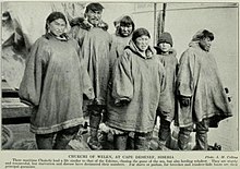 Six people, maybe parents and four children, all wearing long voluminous smock-like outer garments and large boots. Some wear close-fitting hats. Five are staring suspiciously at the camera, one is looking away.