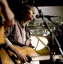 A woman playing guitar and singing into a microphone stand.